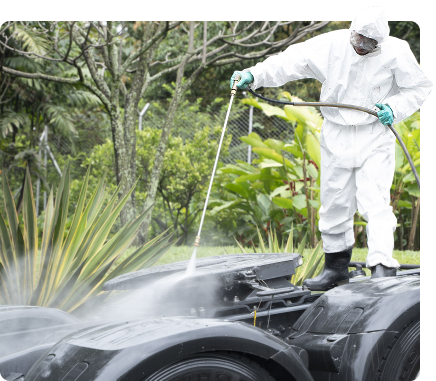 Persona con traje protector y máscara limpiando maquinaria con una manguera a presión.