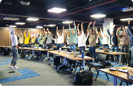 Grupo de personas en una sala de conferencias levantando los brazos como parte de una actividad grupal.