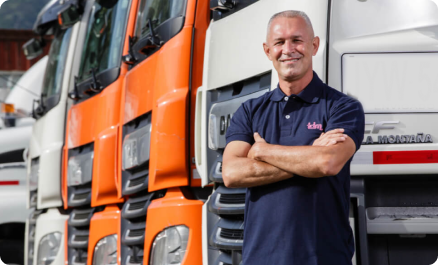Un hombre de pie con los brazos cruzados frente a una fila de camiones naranjas y blancos.