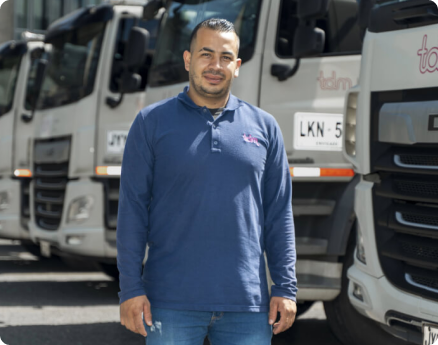 Un hombre con camiseta azul de pie frente a una fila de camiones blancos.