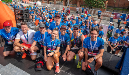 Grupo de corredores sonrientes posando tras una carrera, con medallas y camisetas azules.