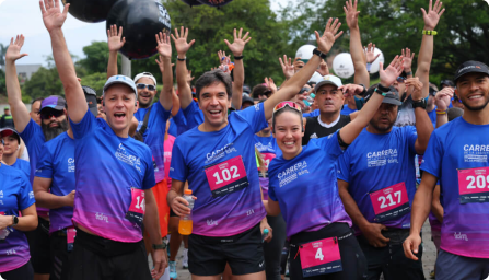 Personas participando en una carrera, vistiendo camisetas azules y sonrientes, con números de dorsal visibles.