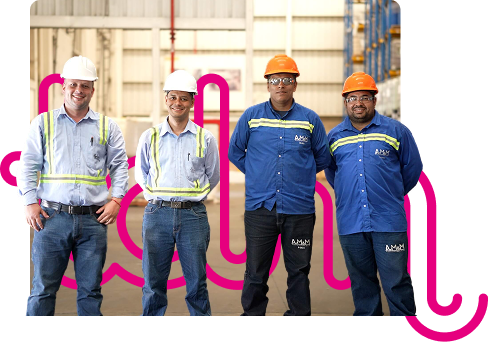 Cuatro trabajadores de una fábrica con cascos y camisas azules, posando sonrientes en un almacén.