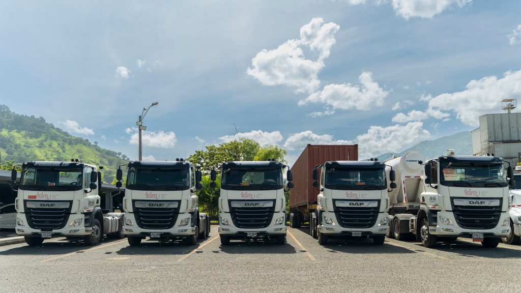 Cinco camiones blancos estacionados en fila bajo un cielo azul con algunas nubes.