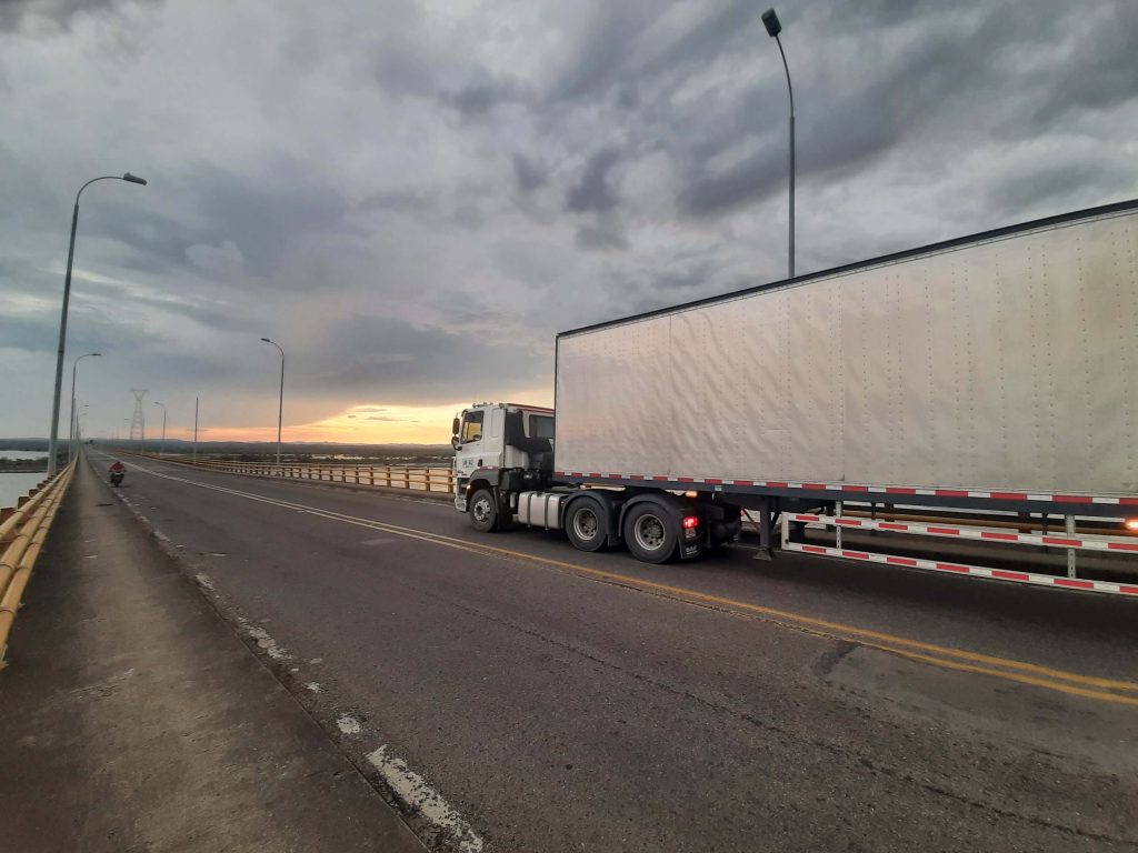 Camión de carga cruzando un puente al atardecer con el cielo parcialmente nublado.