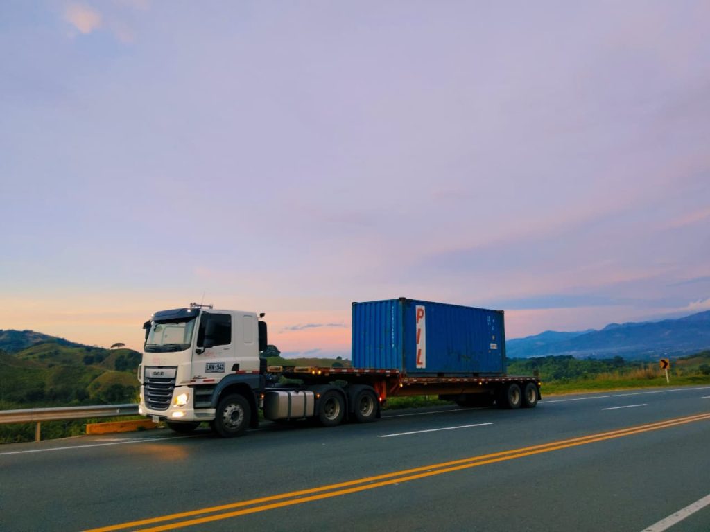 Camión blanco con un contenedor azul en una carretera al atardecer.