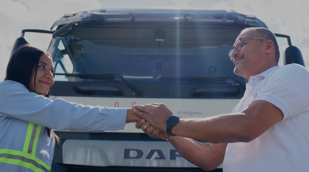 Hombre y mujer estrechándose las manos frente a un camión con la marca "DAF" visible.