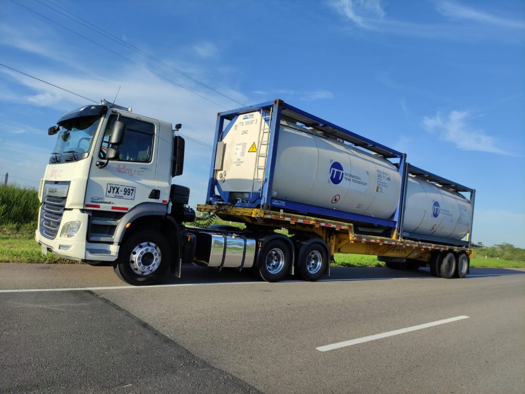 Camión de carga blanca con dos contenedores cisterna en un camino rural bajo un cielo azul.